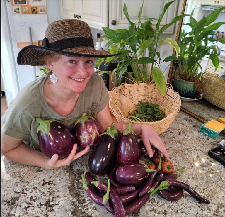 Marion smiling beside a harvest of homegrown eggplants